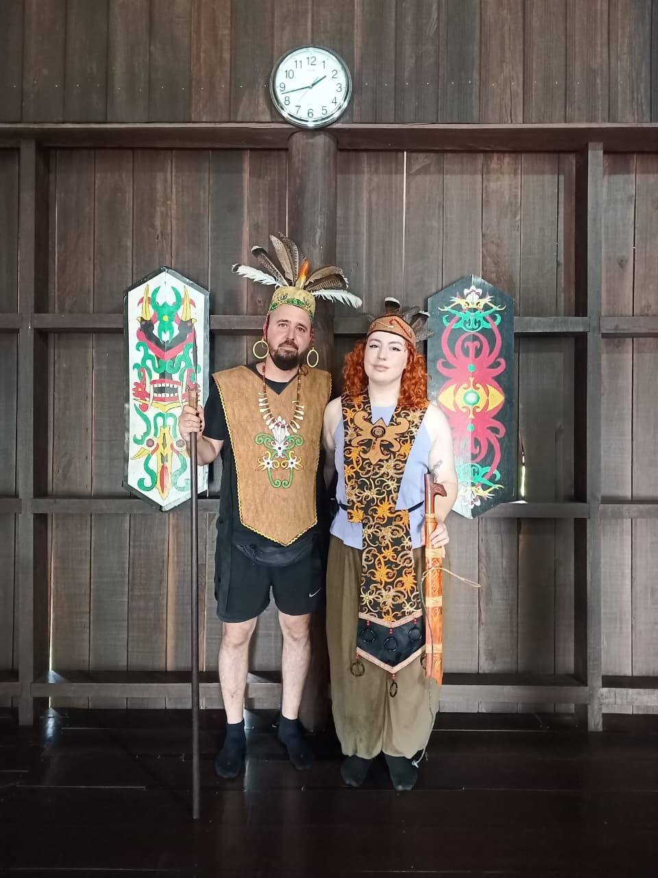 Guests dressed in authentic Dayak warrior and ceremonial attire inside a traditional longhouse.