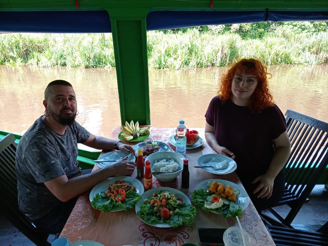 A couple enjoying a freshly cooked local lunch on the klotok deck beside the river.